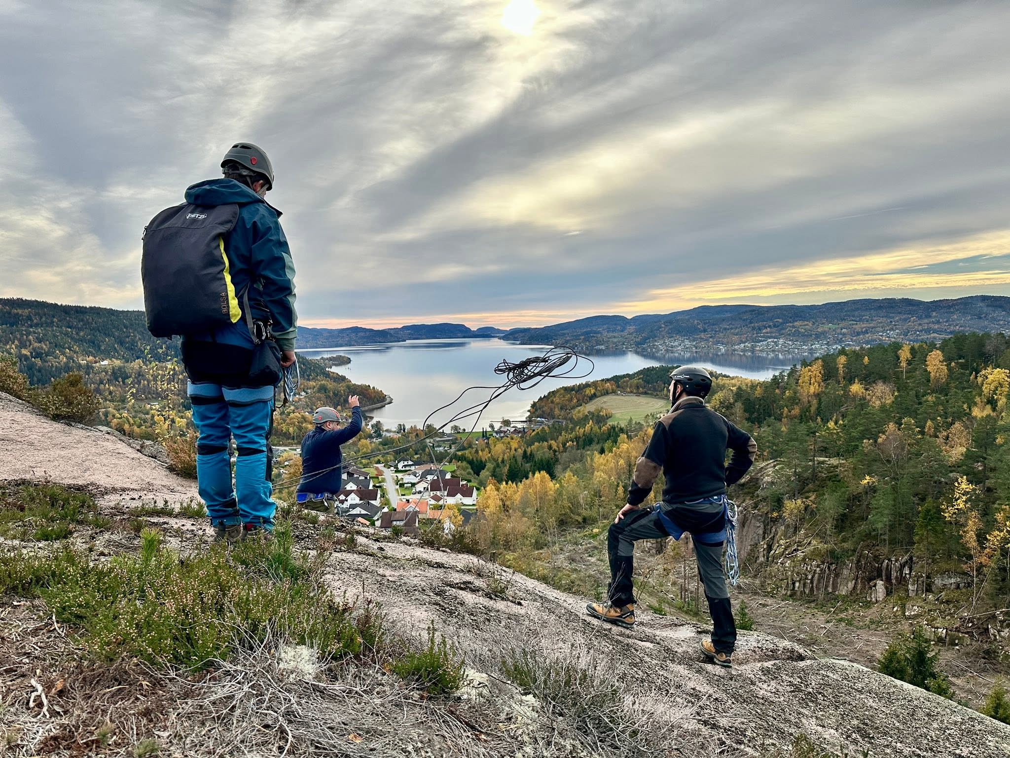 Klatrere med hjelm og tau på fjellet med utsikt over vann og bygd